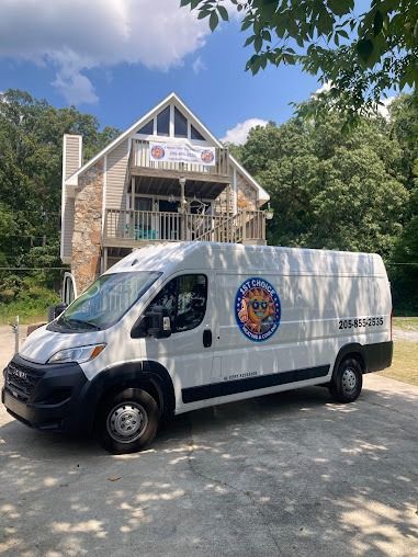 White van with business logo parked in front of a stone and wood building, blue sky backdrop.