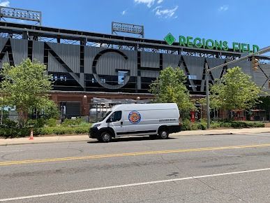 White van parked in front of Regions Field stadium; blue sky overhead.