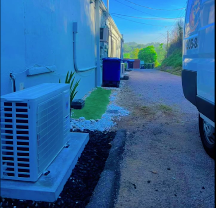 Air conditioning unit next to a white wall, a narrow driveway, and a partially visible van.