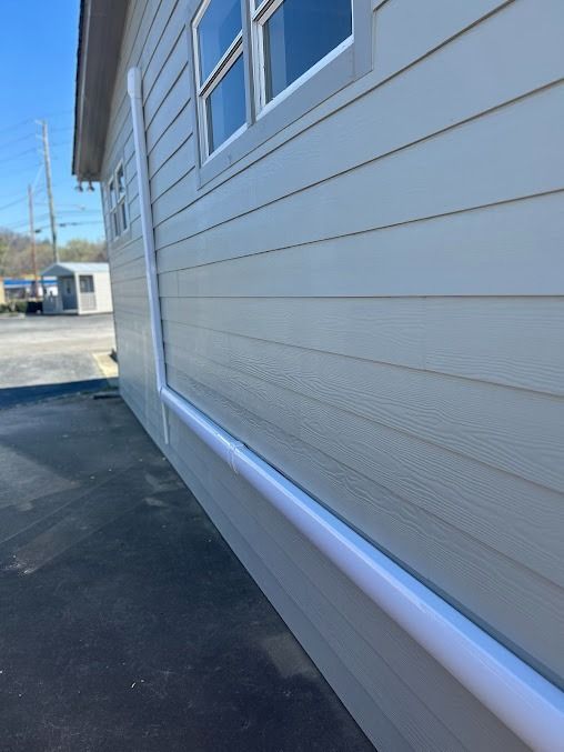 White siding on a building with white pipes running along it. A window is visible.