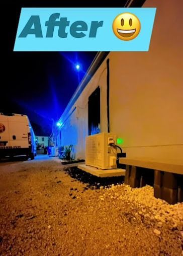 Nighttime view of a building with an air conditioning unit; a service van is in the background. The text 