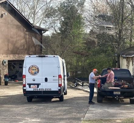 A white van and truck parked outdoors with two men interacting near the vehicles. A building is in the background.