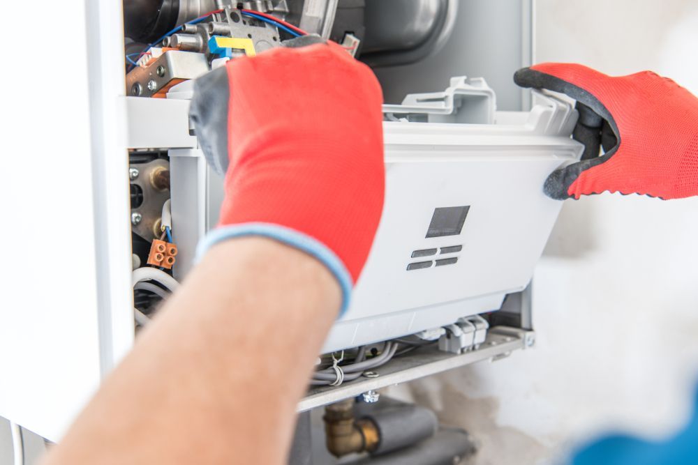 Hands in red gloves installing a white component inside a heating system.