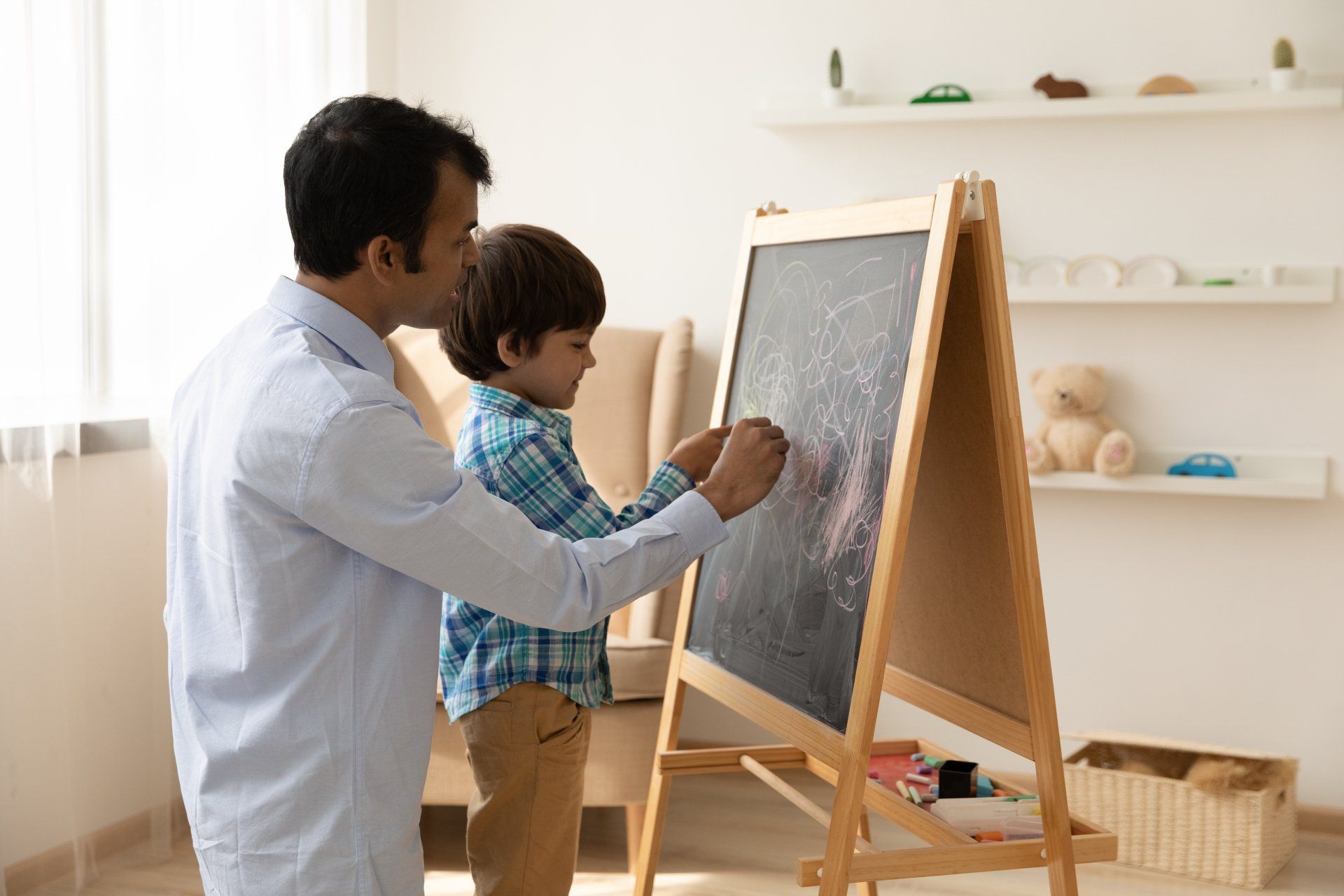 Loving Indian father with little son drawing on black board with colored chalks together