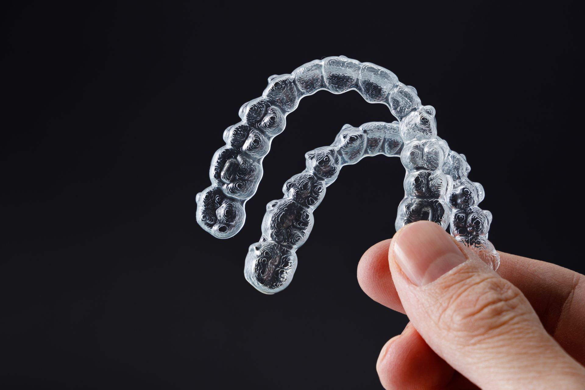 holding clear aligners against black background | Affordable cosmetic Invisalign in Somerset, NJ.