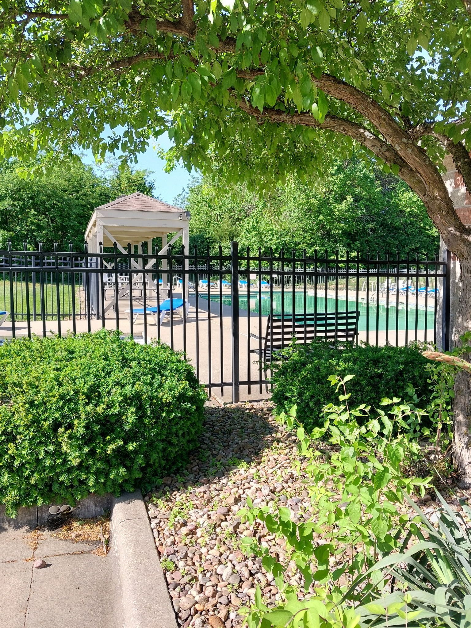 A fence surrounds a swimming pool with a gazebo in the background.
