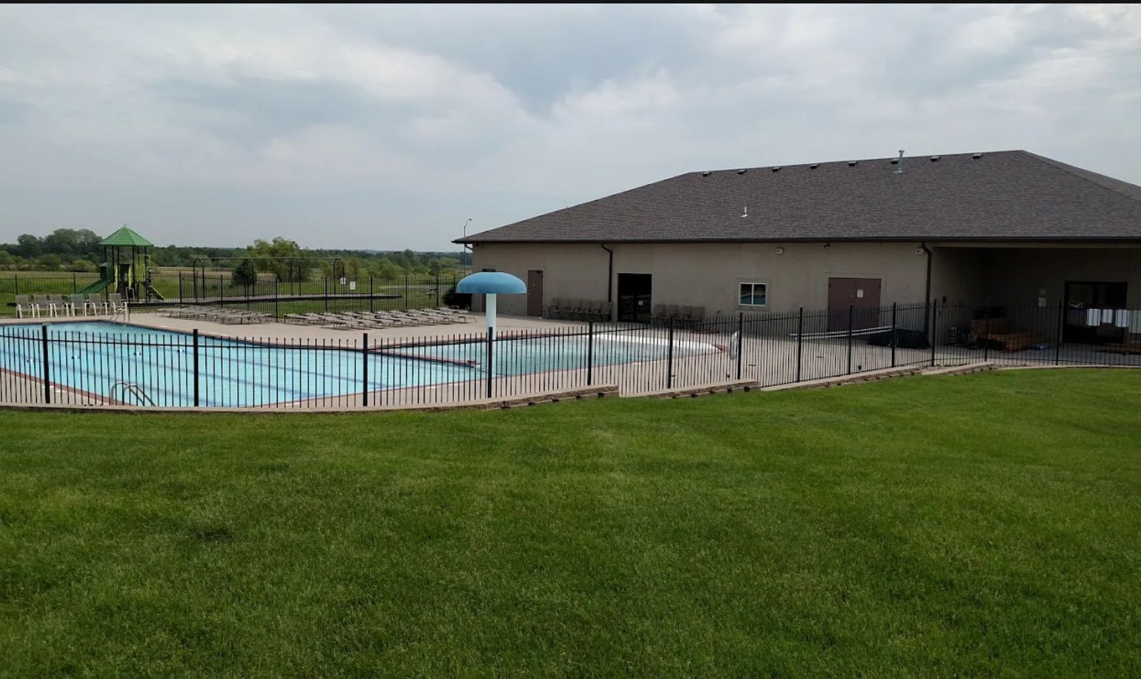 A large swimming pool is surrounded by a fence and a building.