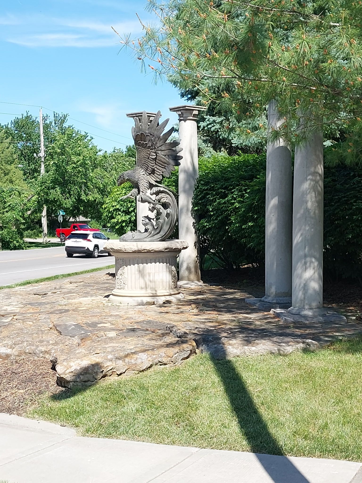 A statue of a phoenix surrounded by columns in a park.