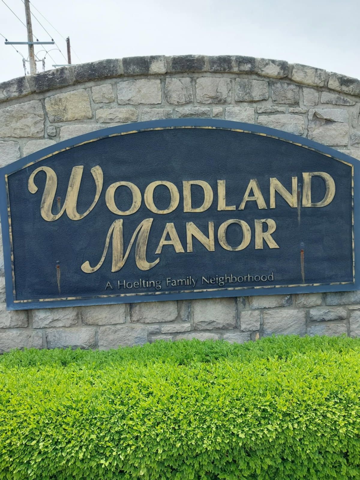 A woodland manor sign is on a stone wall