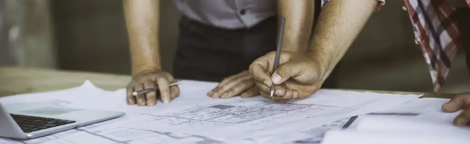 Two people leaning over a blueprint, one is holding a pencil and drawing on the paper.
