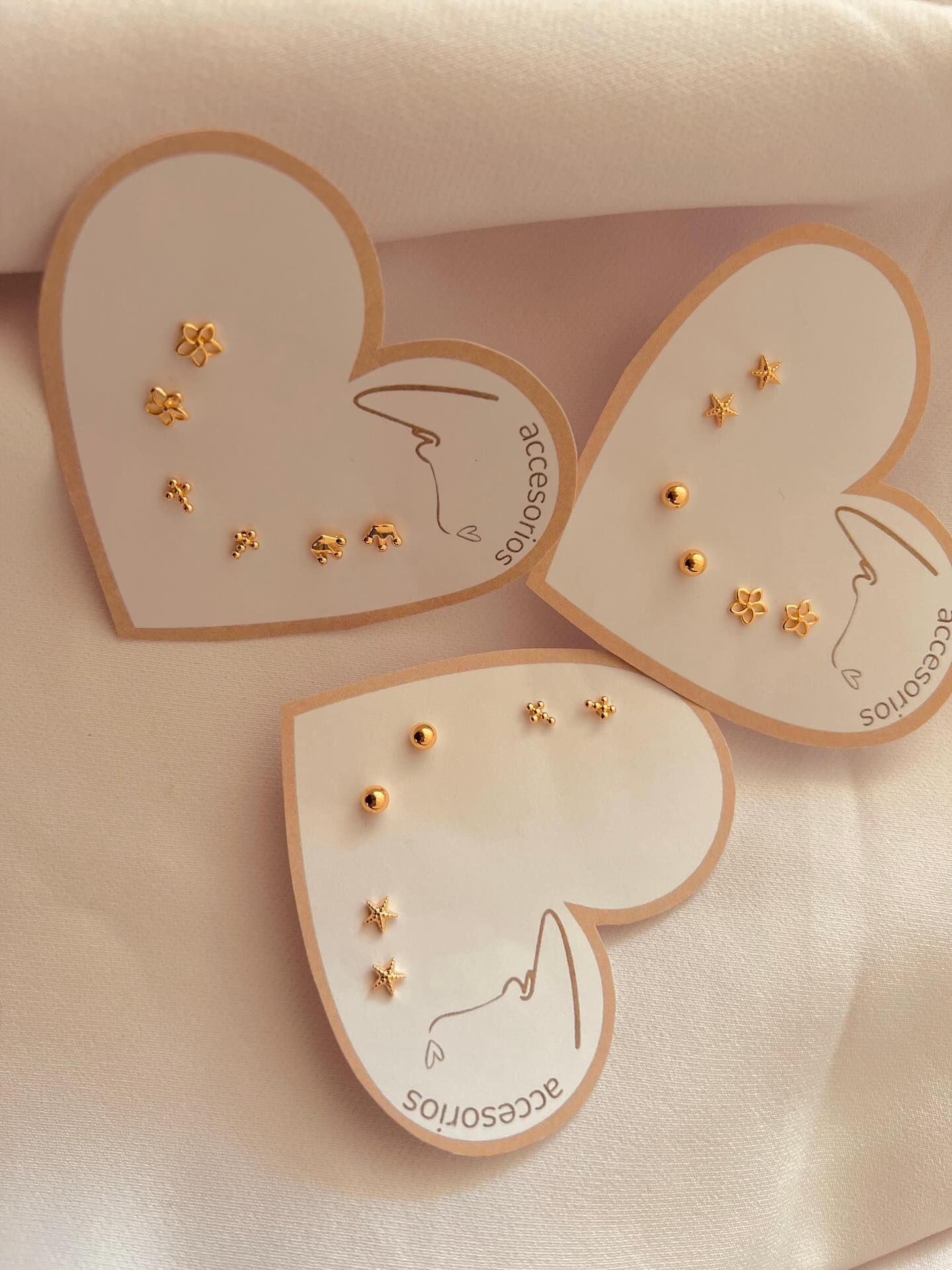 Tres expositores de pendientes en forma de corazón con pendientes dorados dispuestos sobre ellos.