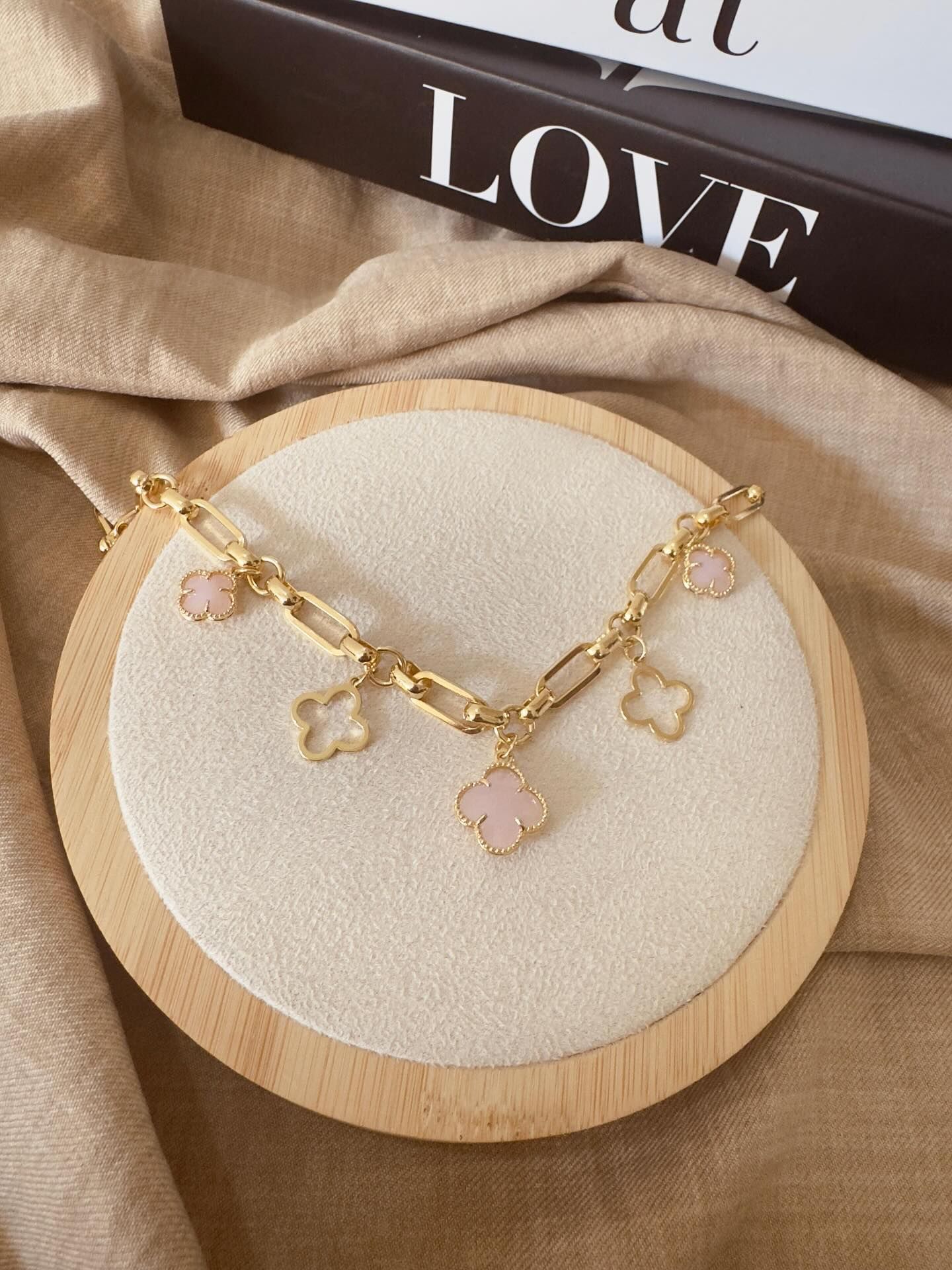 Pulsera de cadena de oro con dijes de trébol rosa y blanco sobre expositor.