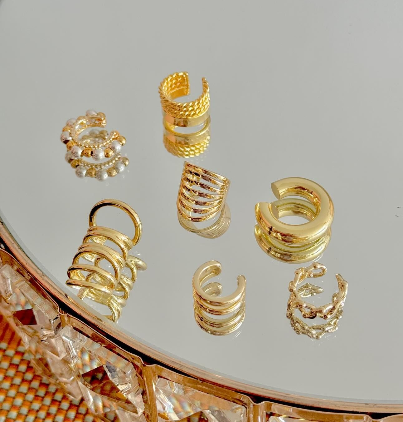 Puños de oreja dorados dispuestos sobre una superficie reflectante.