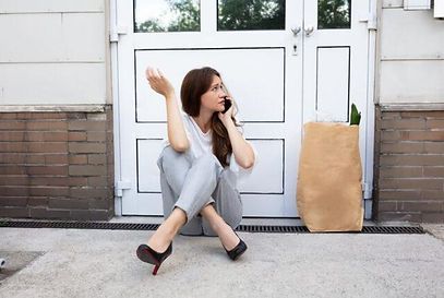 A woman is sitting on the ground in front of a door talking on a cell phone.