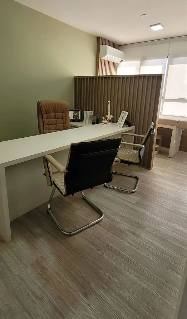 Escritório com uma grande mesa branca, cadeiras executivas e divisória de madeira. Piso claro e paleta de cores neutras.