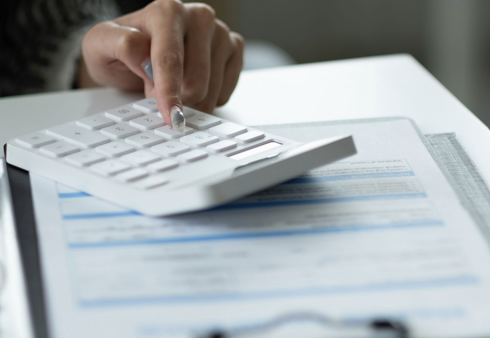 Woman with arms crossed, wearing blue polka dot shirt, standing outside a building, looking directly at the camera.