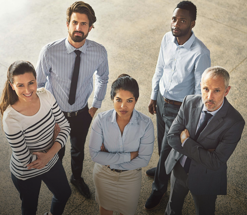 Woman with arms crossed, wearing blue polka dot shirt, standing outside a building, looking directly at the camera.