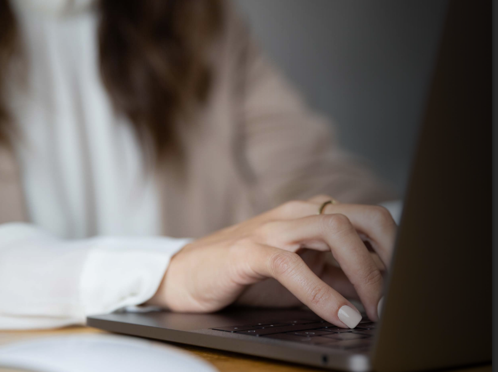 Woman in business suit with arms crossed, smiling, with colleagues in the background.