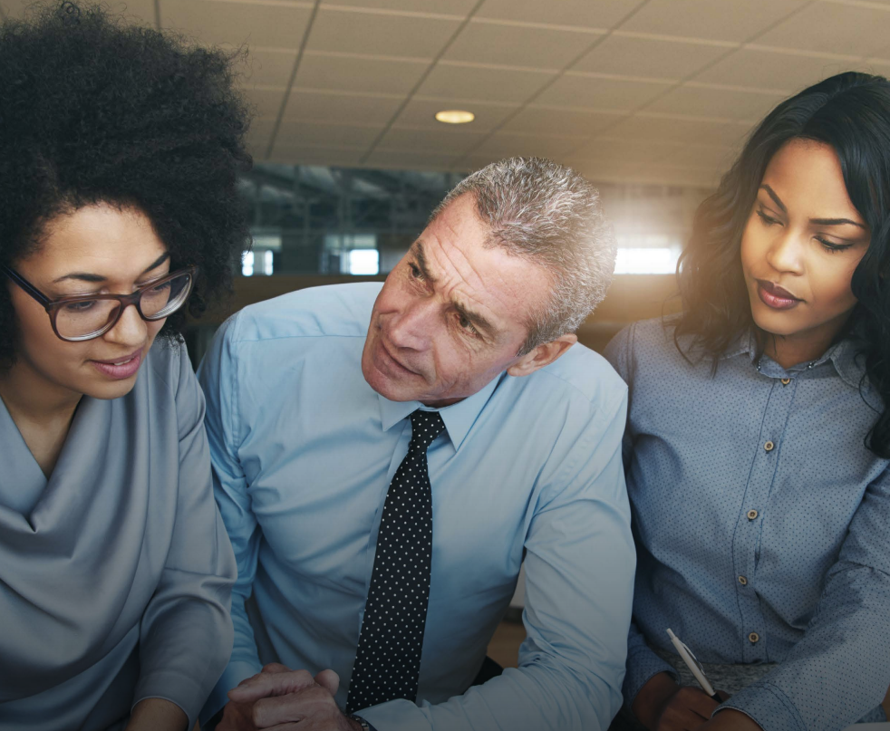 Overhead view of office with four people at desks, some using laptops, papers strewn about.