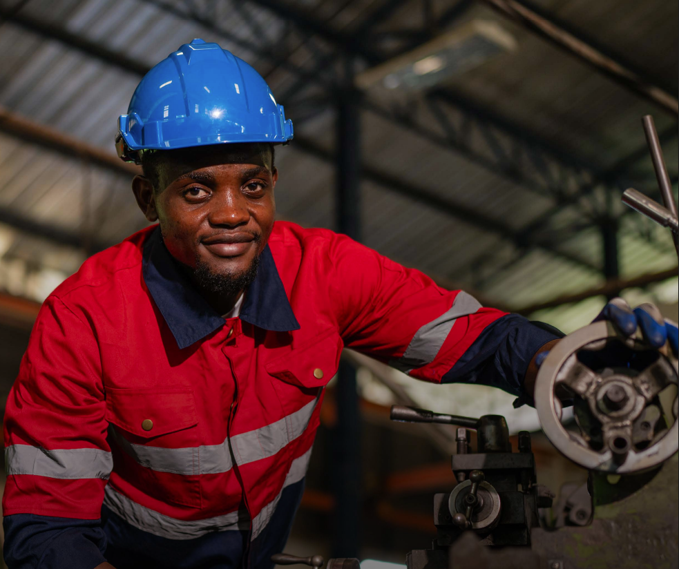 Two people in navy suits, standing in a well-lit office setting. The woman in the front is smiling, hands clasped.