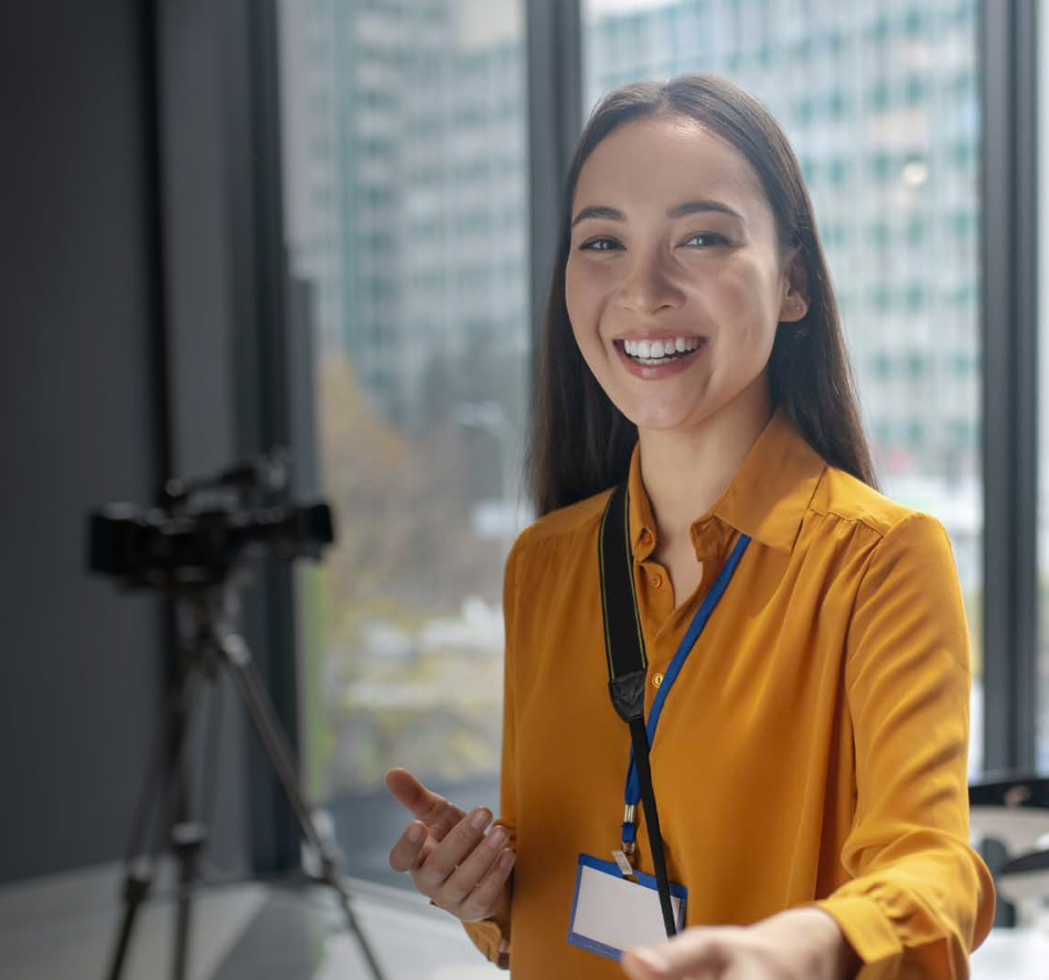 Woman with arms crossed, wearing blue polka dot shirt, standing outside a building, looking directly at the camera.