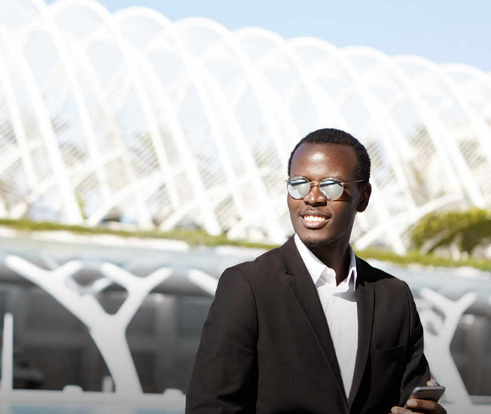 Two people in navy suits, standing in a well-lit office setting. The woman in the front is smiling, hands clasped.