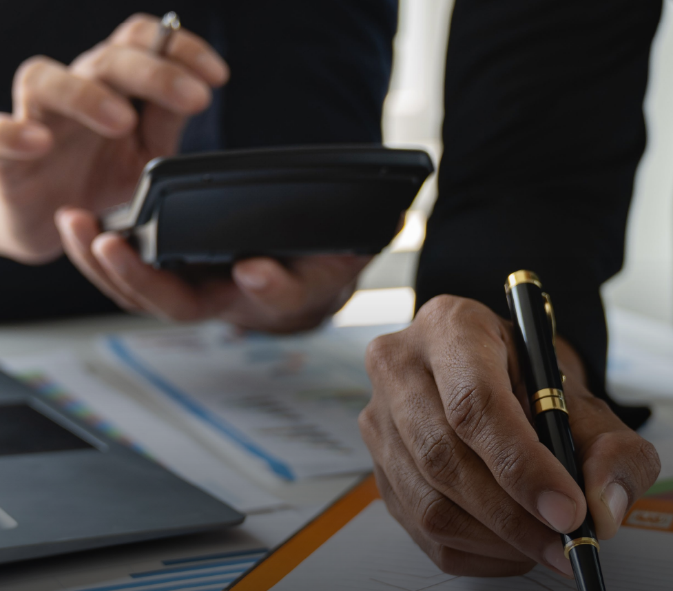 Woman in business suit with arms crossed, smiling, with colleagues in the background.