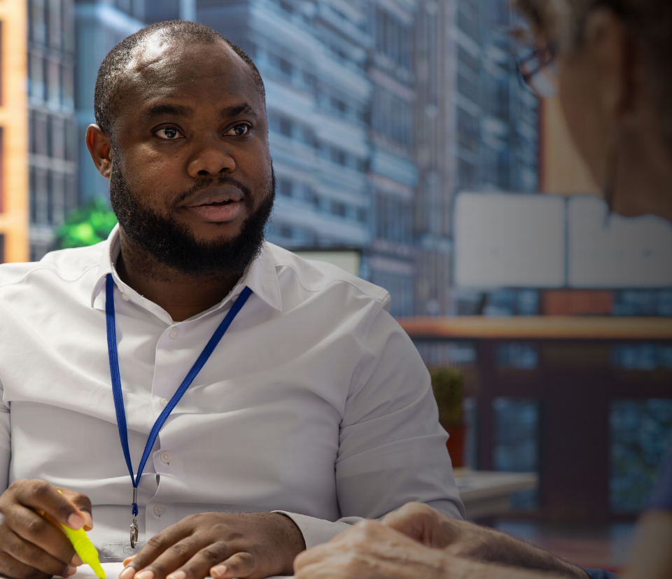 Woman in business suit with arms crossed, smiling, with colleagues in the background.