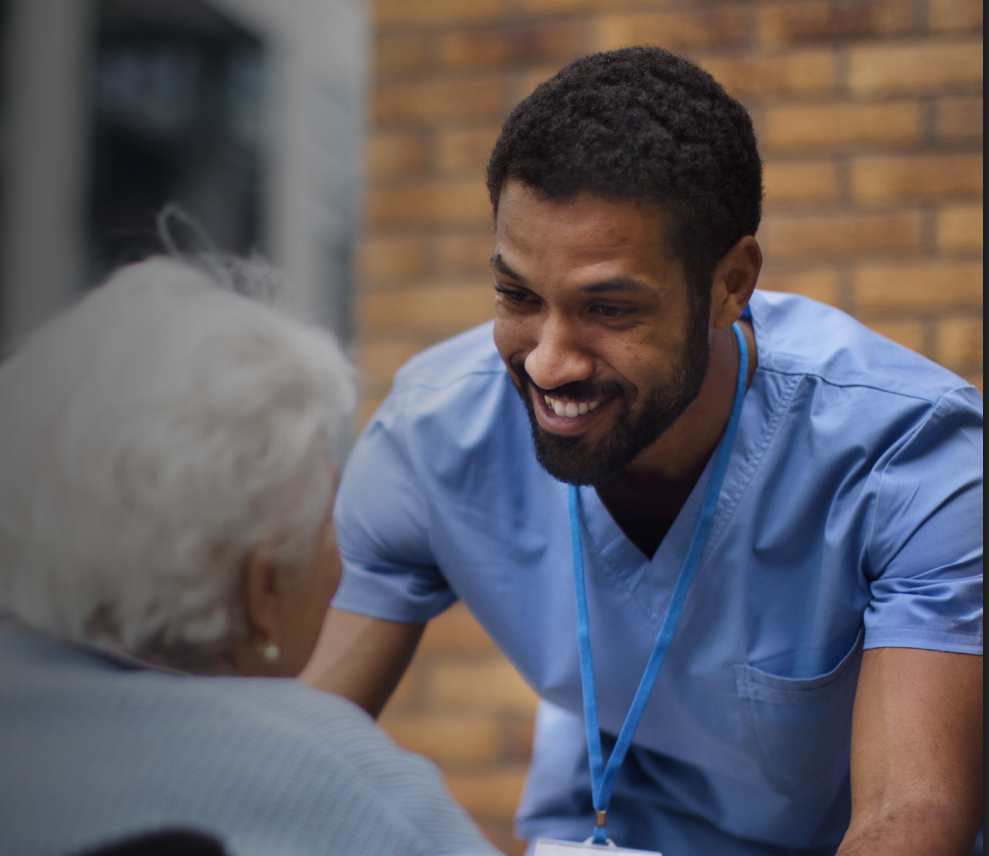 Two people in navy suits, standing in a well-lit office setting. The woman in the front is smiling, hands clasped.
