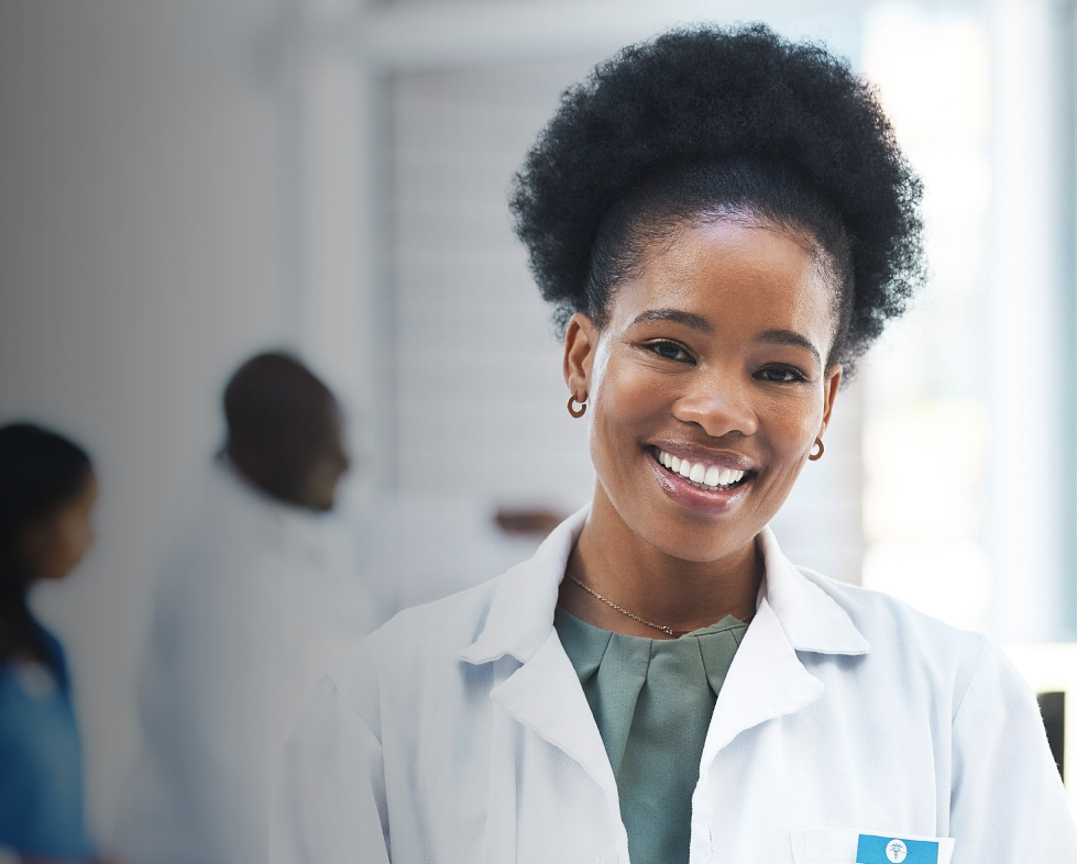 Woman in business suit with arms crossed, smiling, with colleagues in the background.