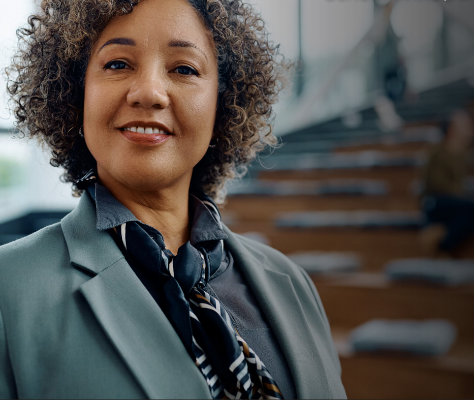 Woman with arms crossed, wearing blue polka dot shirt, standing outside a building, looking directly at the camera.
