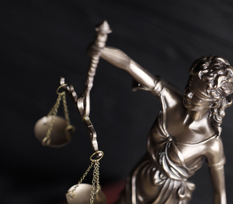 Woman with arms crossed, wearing blue polka dot shirt, standing outside a building, looking directly at the camera.