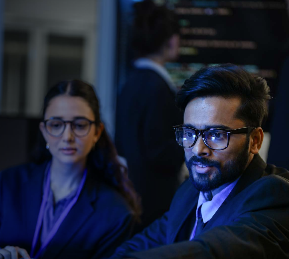 Woman with arms crossed, wearing blue polka dot shirt, standing outside a building, looking directly at the camera.