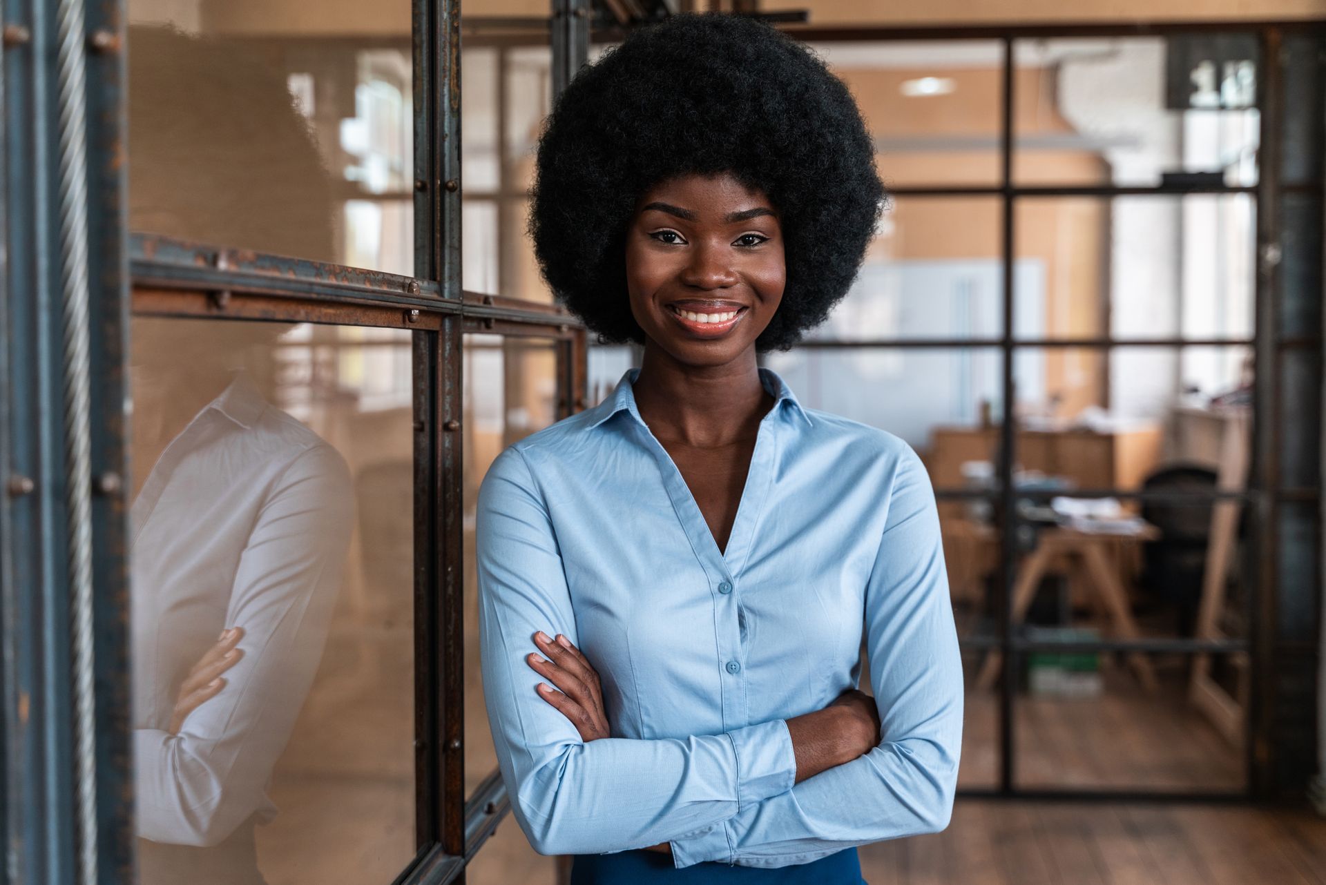 Two people in navy suits, standing in a well-lit office setting. The woman in the front is smiling, hands clasped.