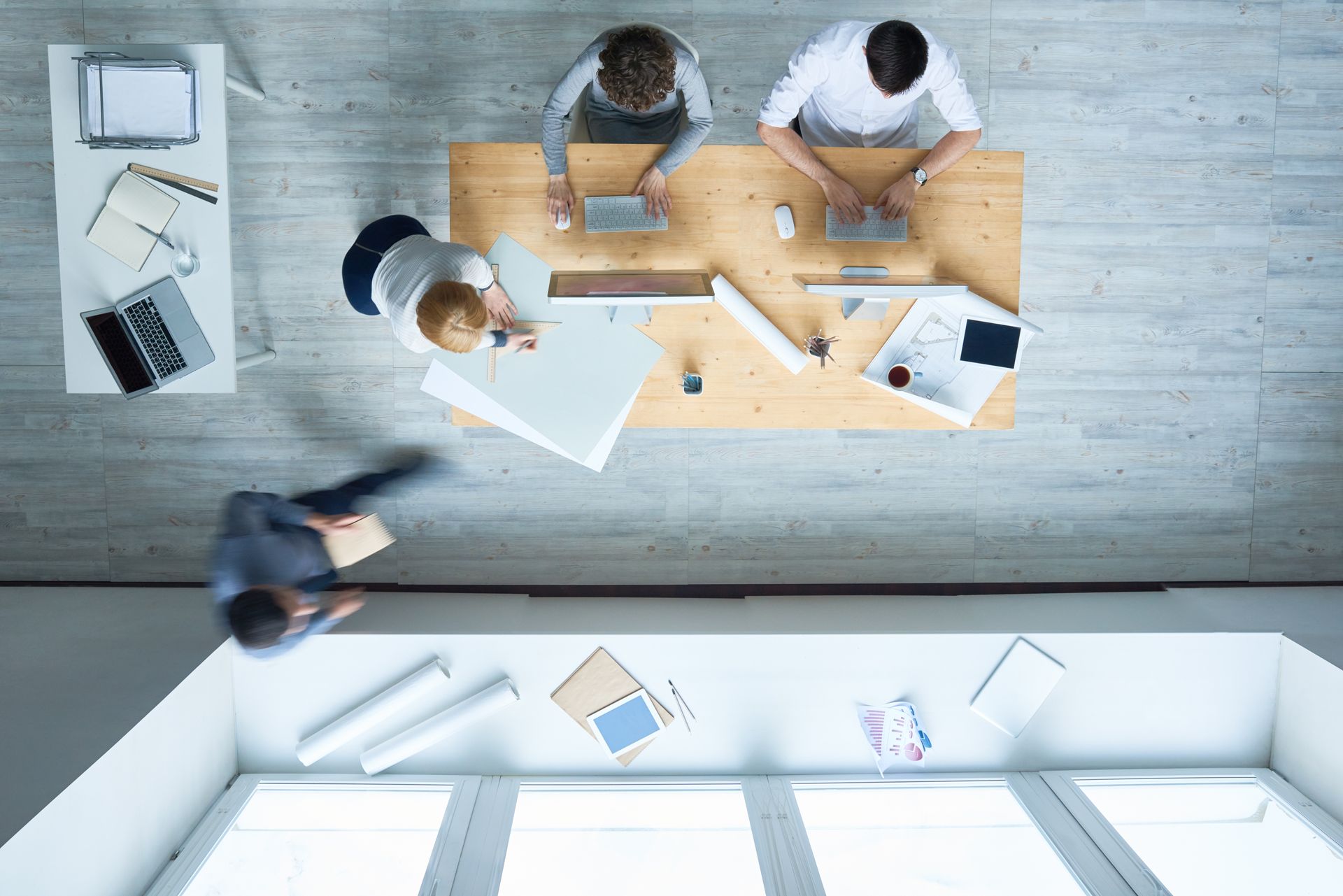 Overhead view of office with four people at desks, some using laptops, papers strewn about.