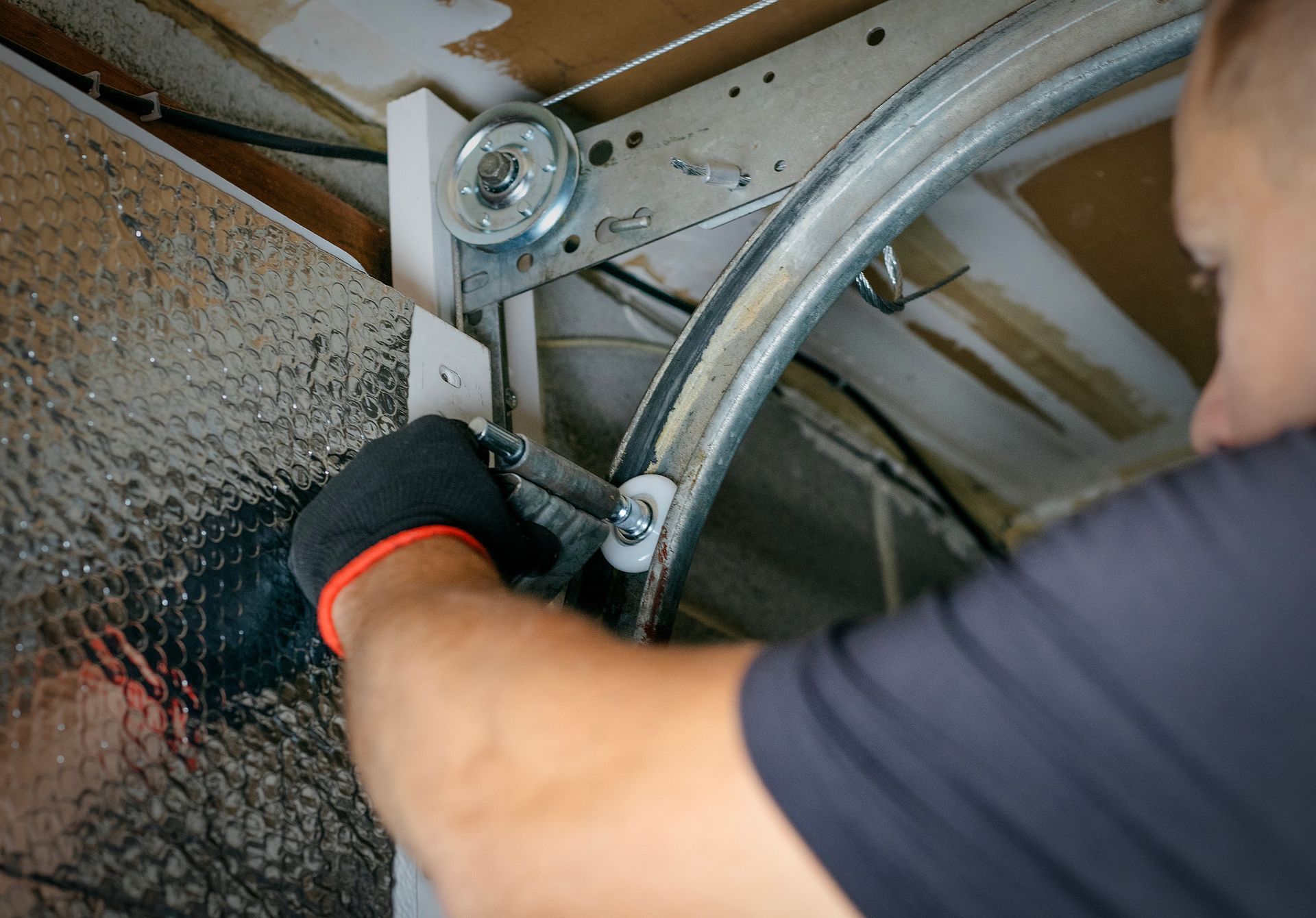 Technician adjusts garage door track with tools, focusing on roller and frame components.