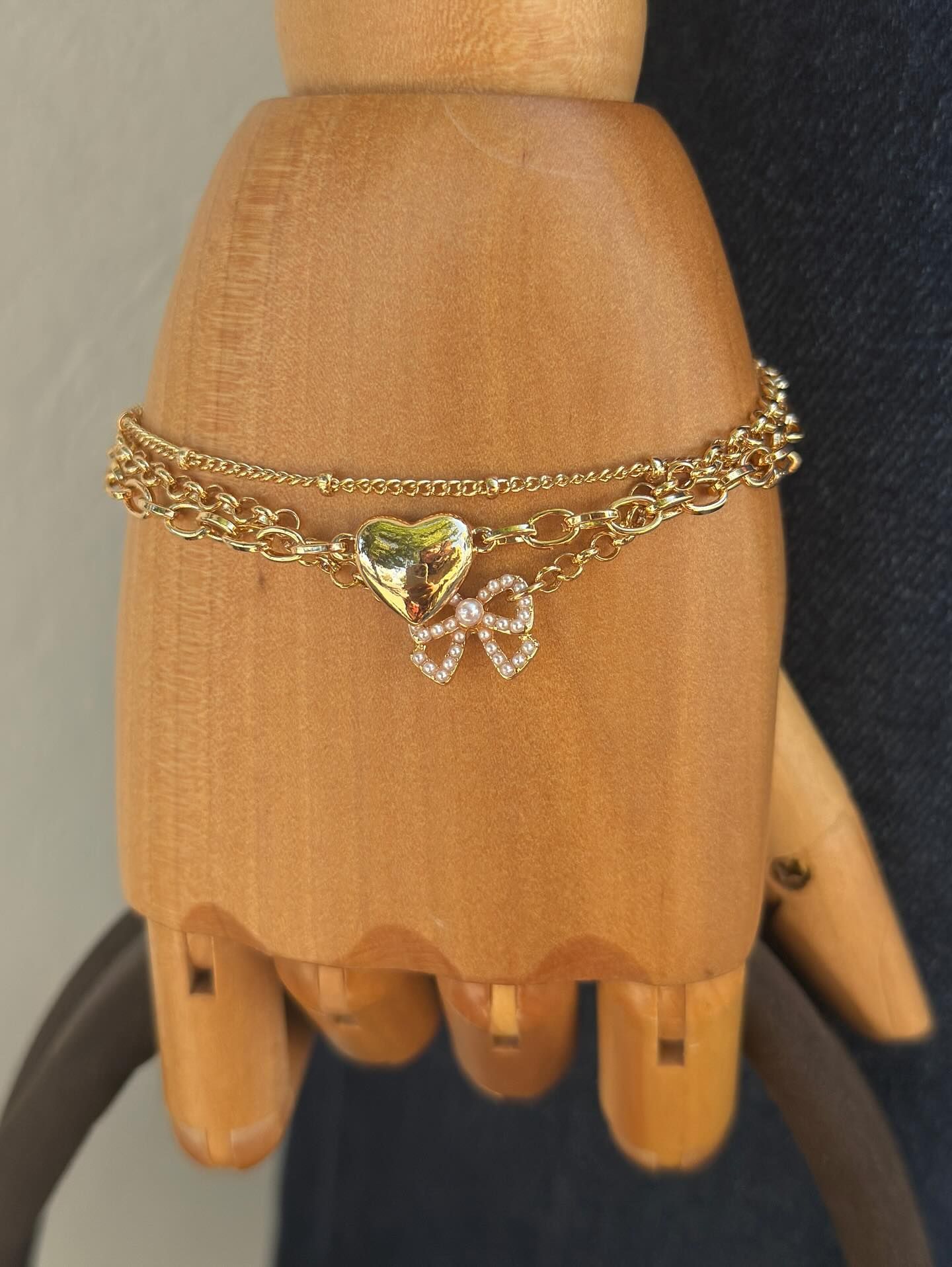 Wooden mannequin wrist wearing a gold chain bracelet with a heart charm and dangling gems