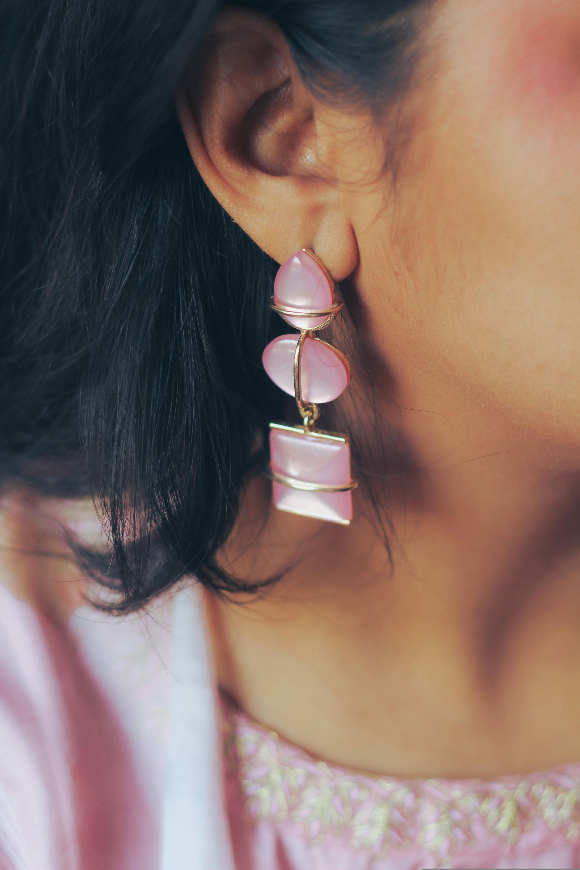 Close-up of a woman wearing a pink gemstone dangle earring and a pink embroidered top