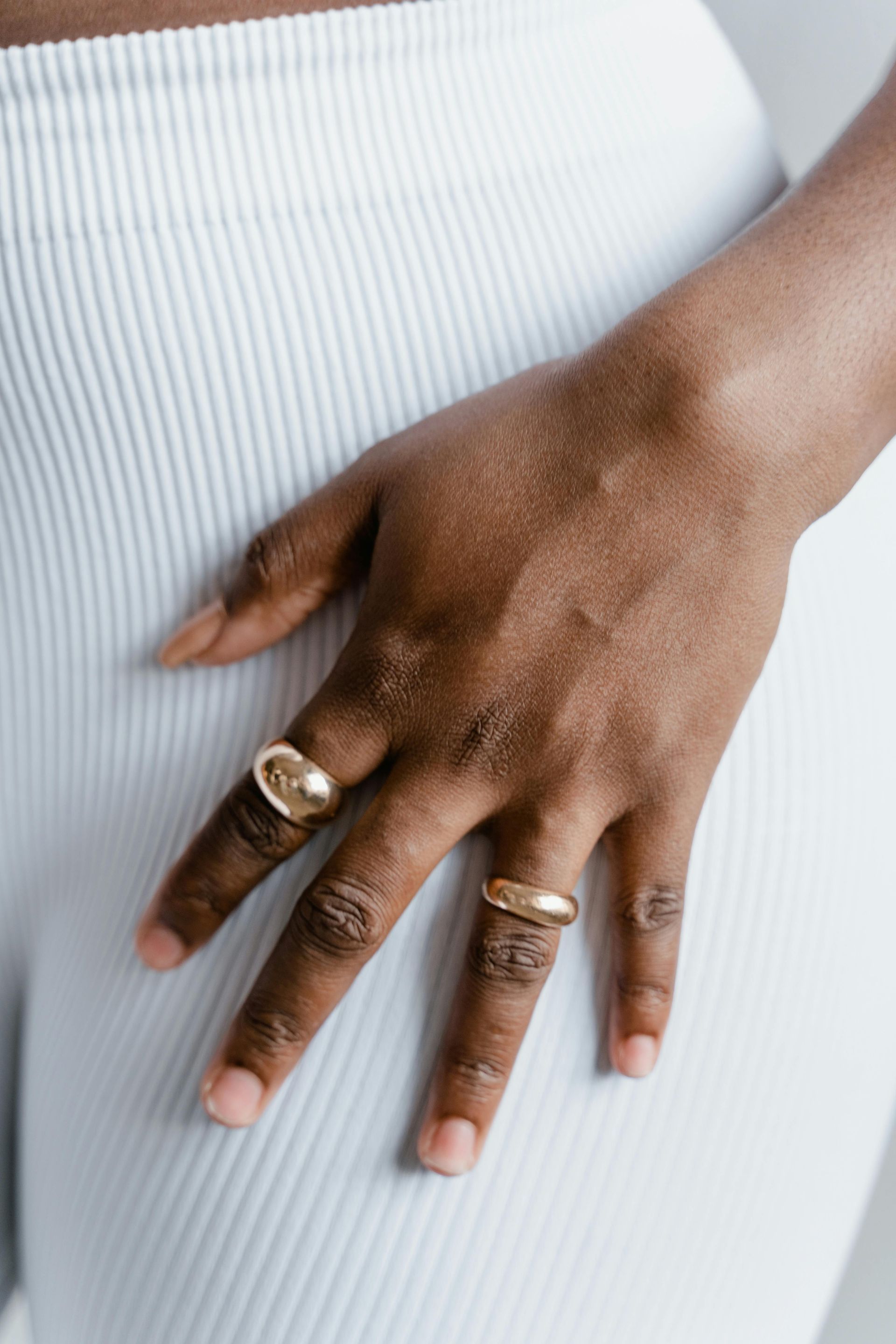 Hand with gold rings resting on white ribbed fabric