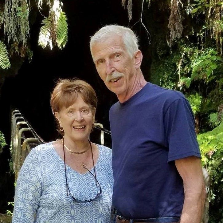 A man and a woman are posing for a picture in front of a cave