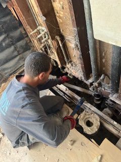 A man is kneeling down in front of a wall holding a wrench.