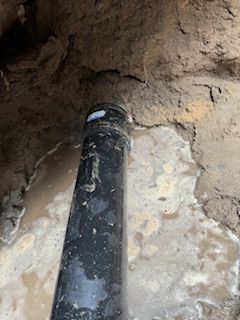 A black pipe is sitting in the dirt next to a wall.