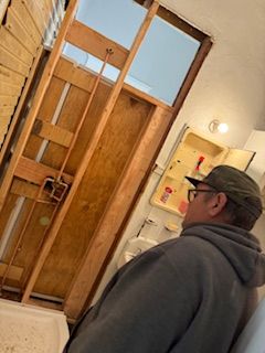 A man is standing in a bathroom looking at a door.