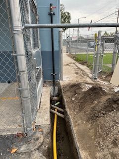 A yellow pipe is being installed in a trench next to a chain link fence.