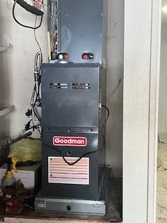 A goodman air conditioner is sitting in a closet next to a wall.