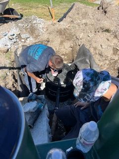 Two men are working on a septic tank in the dirt.