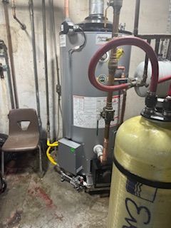 A water heater is sitting in a basement next to a gas tank.