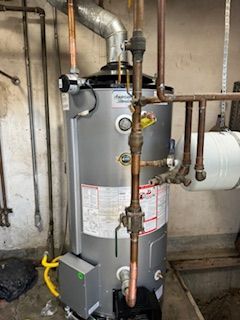 A water heater is sitting in a room next to pipes.