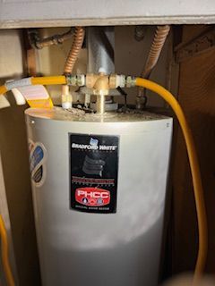 A gas water heater is sitting under a sink with a yellow hose attached to it.