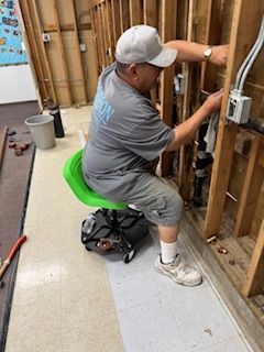 A man is sitting on a green chair working on a wall.